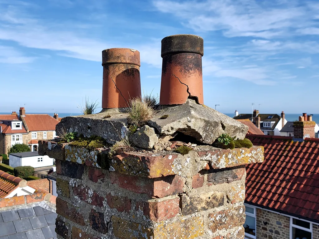 Cracked mortar flaunching around the pots on a brick chimney