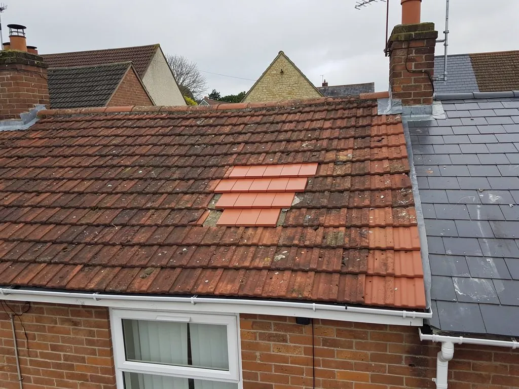 A patch of new clay tiles let into a weathered tiled roof